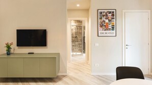A modern living room with a flat-screen TV, a framed Beatles poster, a dining area, and a hallway leading to a bathroom. - GuestHost - New, bright and comfortable apartment near the Ospedale Maggiore and just a few minutes drive from the historic center of Bologna.The neighborhood is full of restaurants, bars and supermarkets and pharmacy.Easily accessible from the motorway  (Bologna)