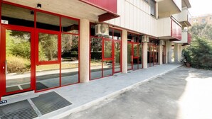 A building with red-framed glass doors, a concrete ground floor, and a white upper section. - GuestHost - New, bright and comfortable apartment near the Ospedale Maggiore and just a few minutes drive from the historic center of Bologna.The neighborhood is full of restaurants, bars and supermarkets and pharmacy.Easily accessible from the motorway  (Bologna)