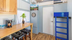 Een kleine keuken met een koffieapparaat, een houten tafel en barstoelen.