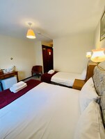 Habitación de hotel con dos camas, un escritorio, una silla y un refrigerador pequeño.
