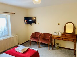 Habitación de hotel con cama, dos sillas, cómoda de madera, televisor y ventana con cortinas.