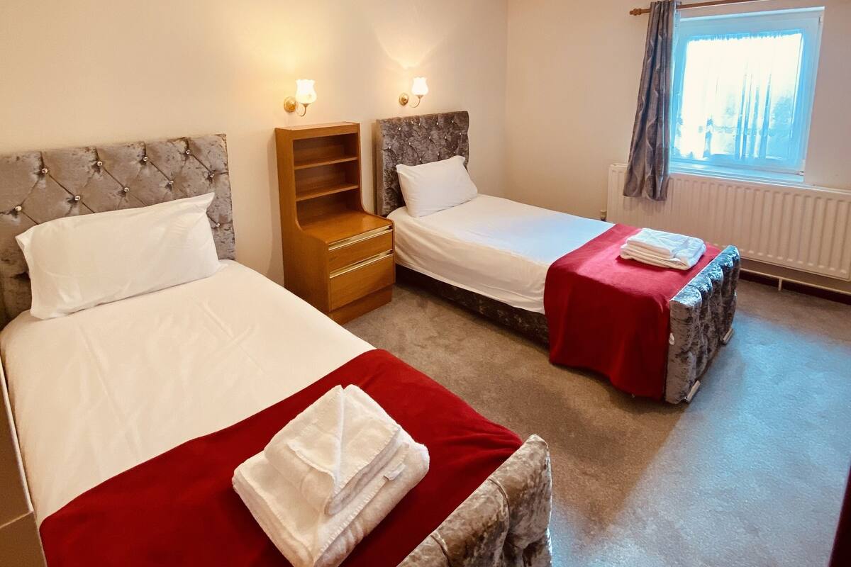 A hotel room with two beds, a wooden nightstand, a marble headboard, and a window with curtains.