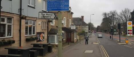 A street view with a sign for The Manor Surgery, a Shell gas station, and a hospital.