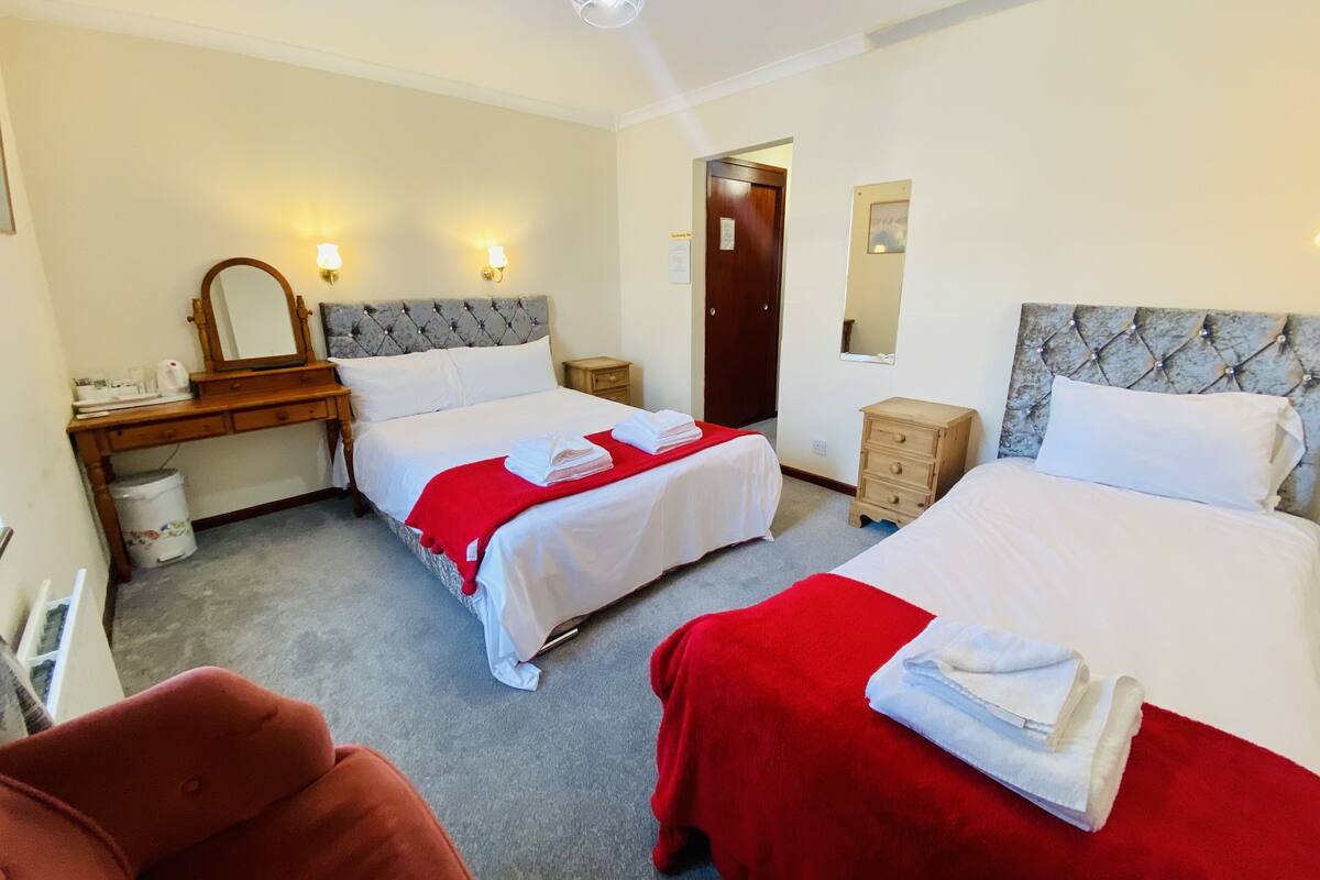 A hotel room with two beds, a desk, a chair, a wardrobe, and a bathroom door.