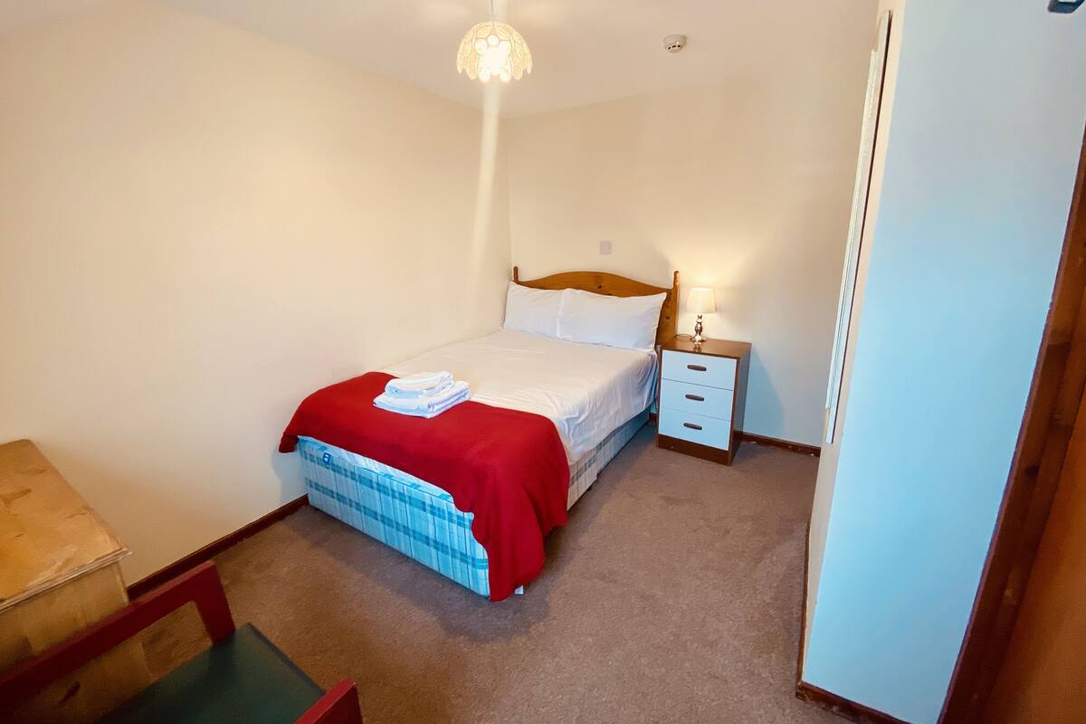 A bedroom with a single bed, a nightstand, a lamp, a radiator, and a chair.