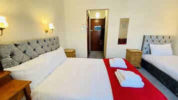 A hotel room with two beds, a wooden nightstand, a red throw blanket, and a mirror on the wall.