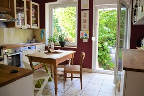 Une cuisine avec des meubles de rangement en bois, une table à manger, des chaises et une fenêtre donnant sur un paysage verdoyant.