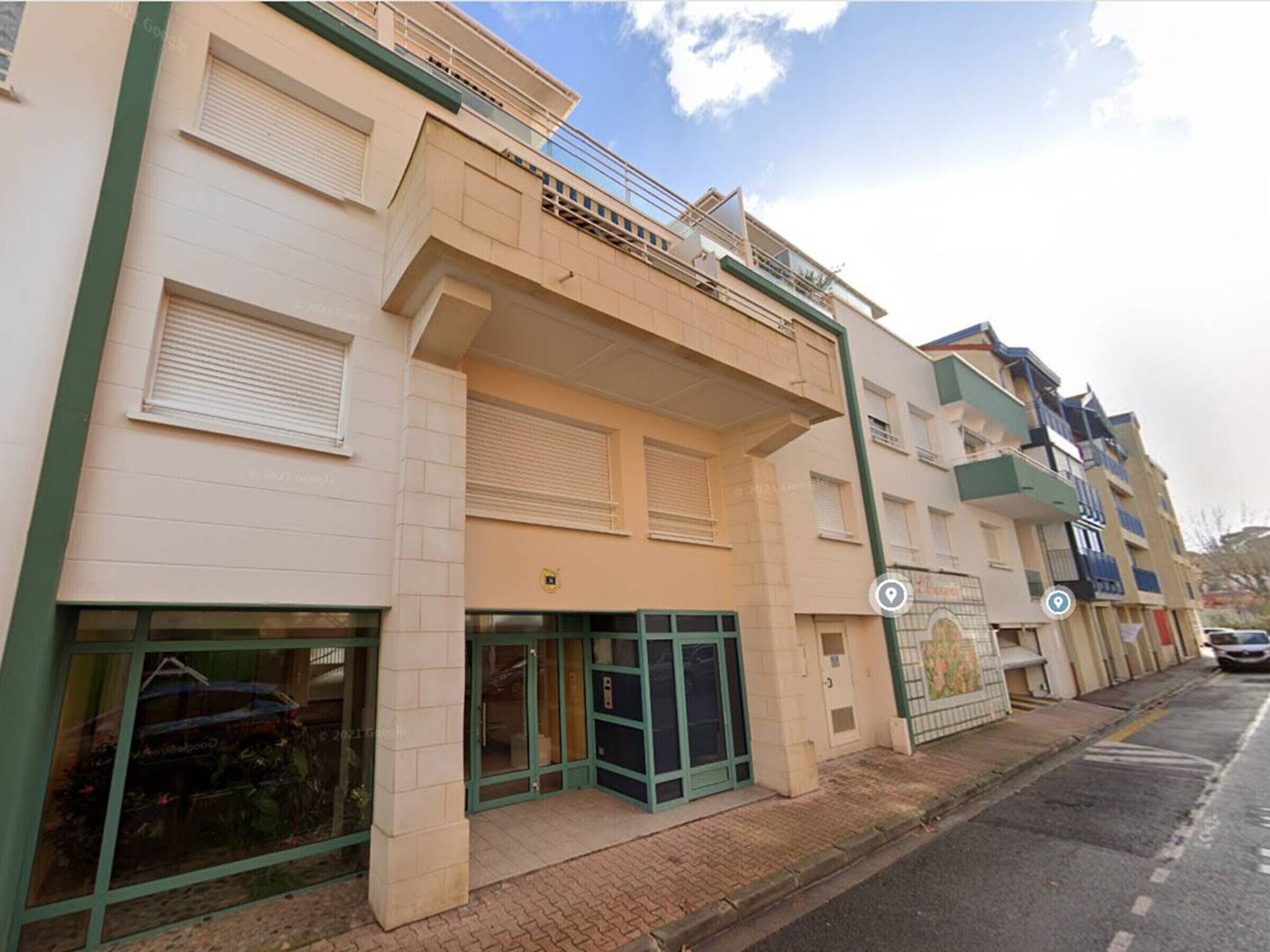 A multi-story residential building with a ground-level entrance, a balcony, and a visible window with a reflection.