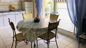 A dining area with a table set for four, surrounded by chairs with a yellow and blue pattern. A basket of fruit is on the table. - Central Arcachon: 400m from Beach, T2 with Balcony, Parking, and Pet-Friendly (Arcachon)