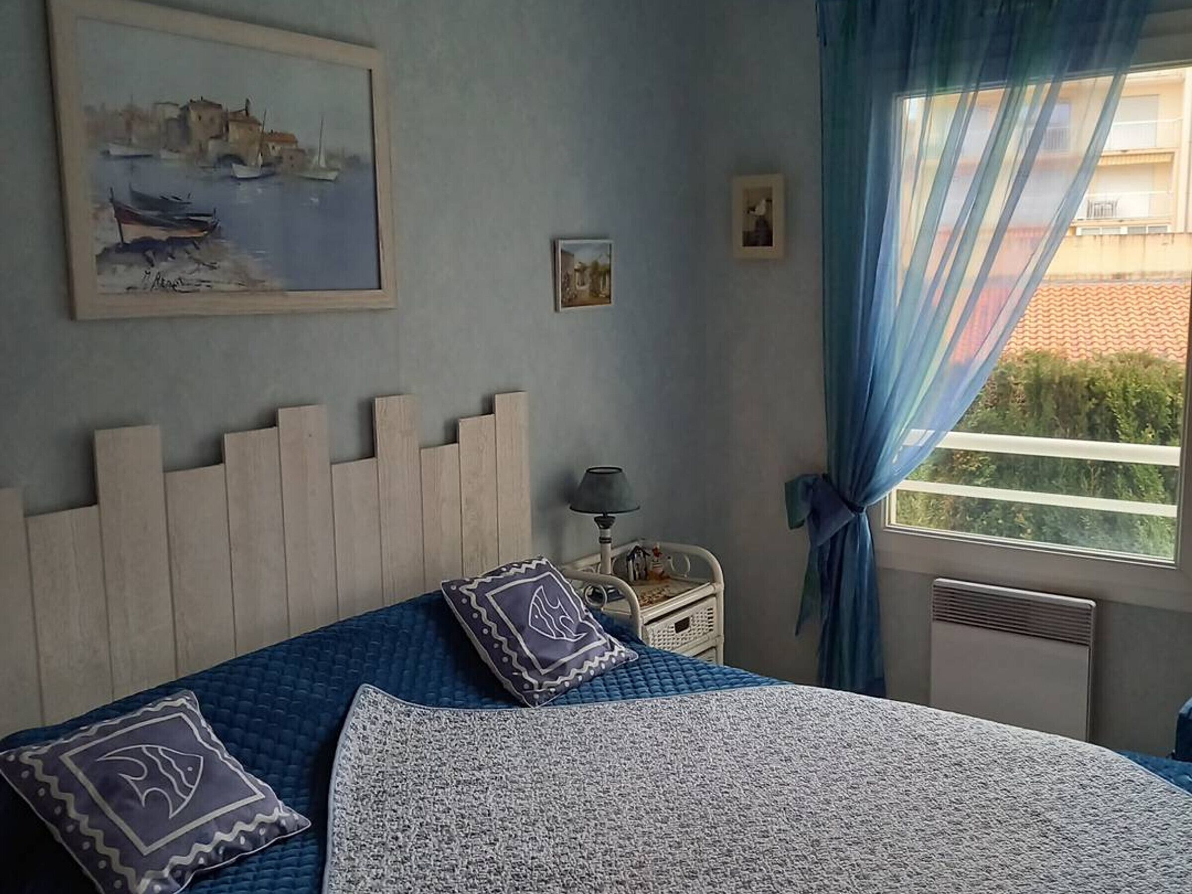 Une chambre à coucher avec un lit, une table de chevet, une lampe, une fenêtre avec des rideaux et un tableau au mur.