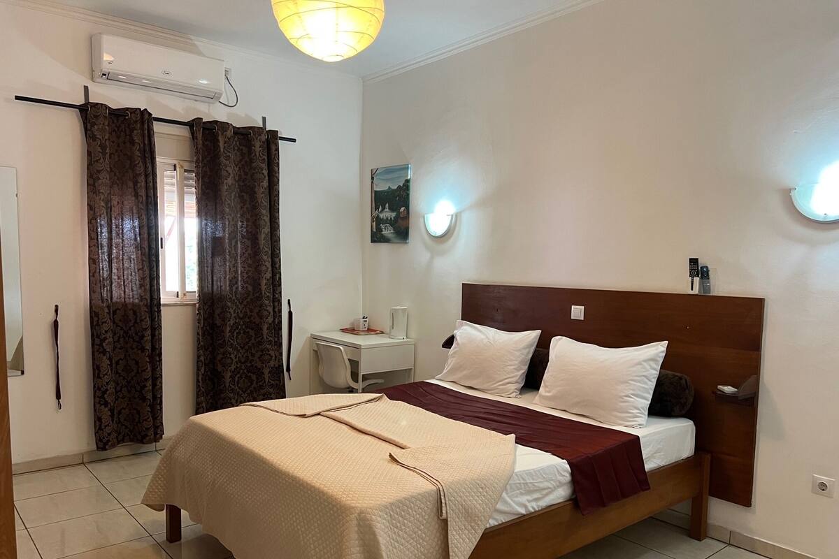 Hotelkamer met een bed, een bureau, een stoel, een raam met gordijnen, een airconditioning en een wandlamp.