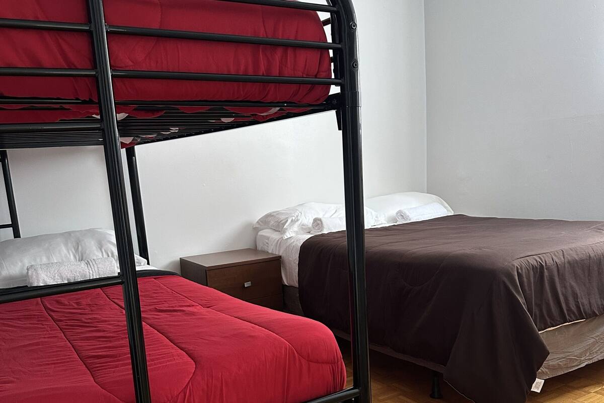 Une chambre avec un lit superposé, un lit simple, une table de chevet et un plancher en parquet.