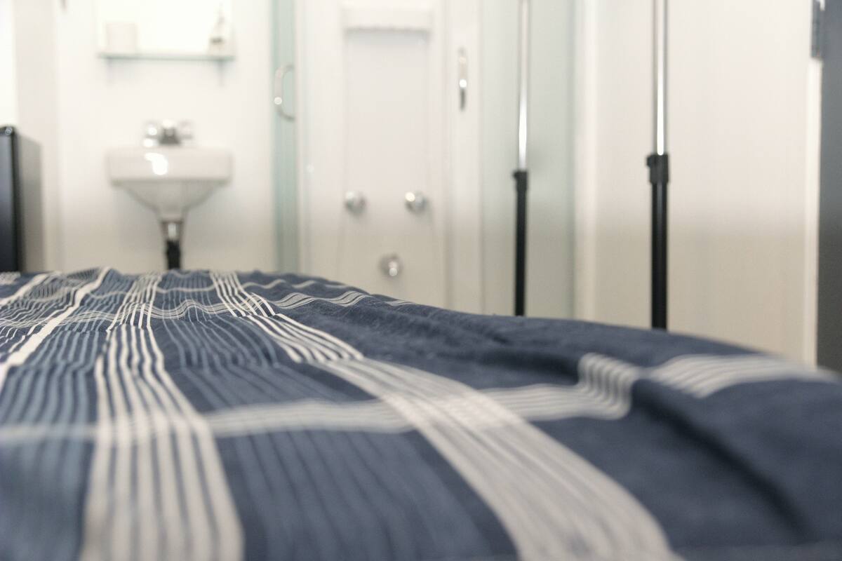 Un lit avec une couverture à rayures, un lavabo blanc et une porte dans une chambre d’hôtel.