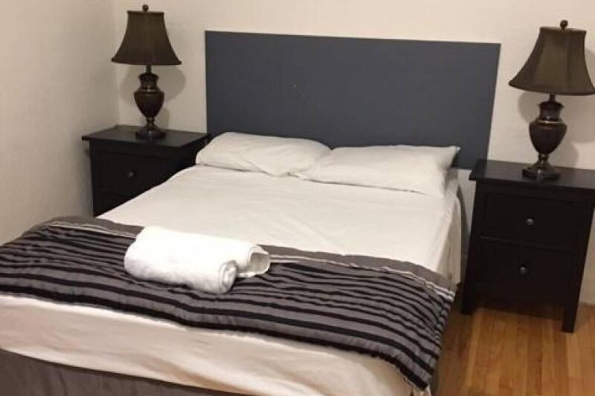 Un lit simple avec une tête de lit sombre, deux tables de chevet avec des lampes et un plancher en bois.