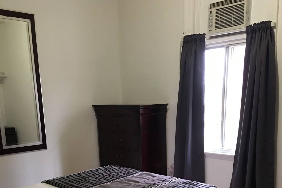 Une chambre à coucher avec un lit, une commode, un miroir et une fenêtre avec des rideaux.