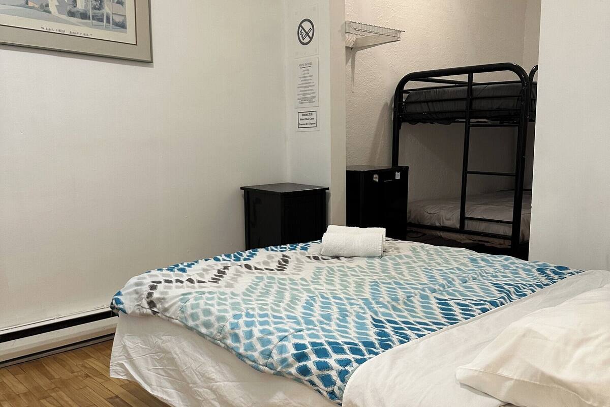 Une chambre avec un lit superposé, un tableau encadré au mur, une armoire noire et un plancher en bois.