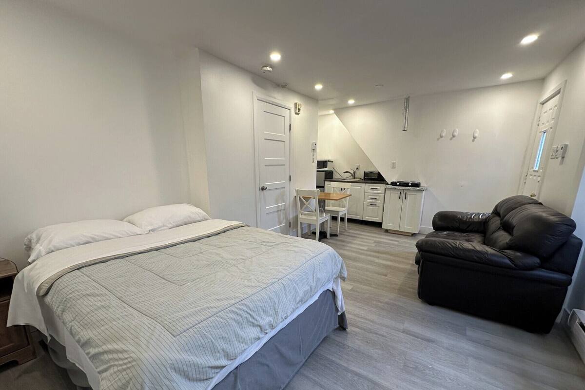 Une chambre à coucher avec un lit, une chaise, un canapé et, au fond, une petite cuisine.