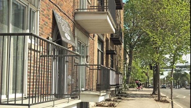 Un hilera de casas adosadas de ladrillo con balcones, una acera despejada y un ciclista a lo lejos.