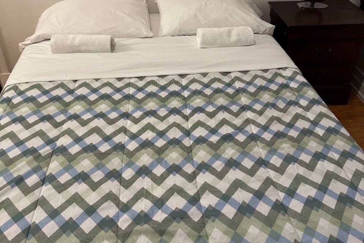 Un lit avec une couvre-lit à motifs, des oreillers blancs et une table de chevet avec une lampe.