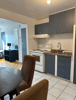 A compact kitchen with a stove, sink, and dark cabinets. There is a dining area with a table and chairs. - Hotel Mini (Montreal)