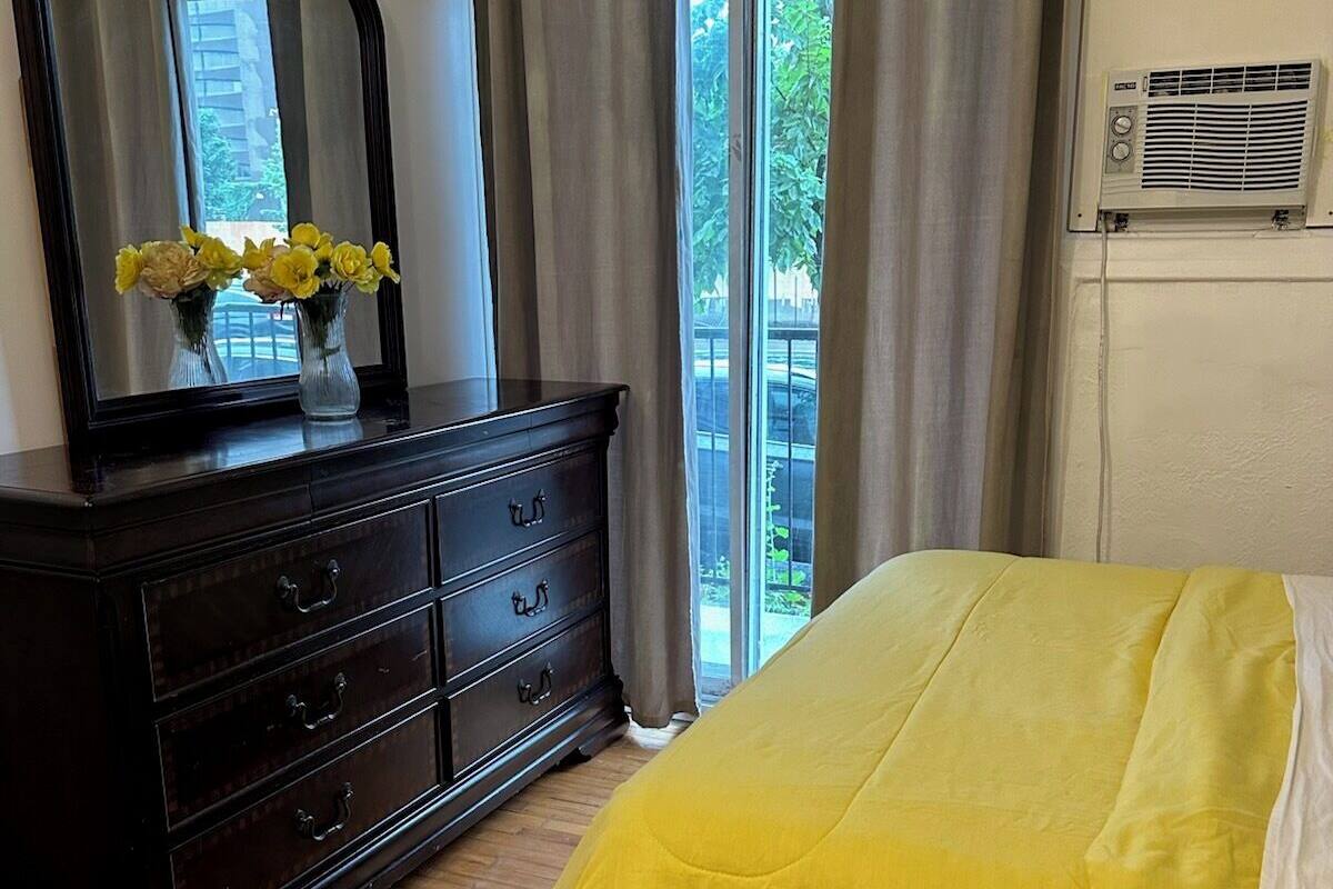 Une chambre à coucher avec un lit, une commode, un miroir et une fenêtre avec des rideaux.
