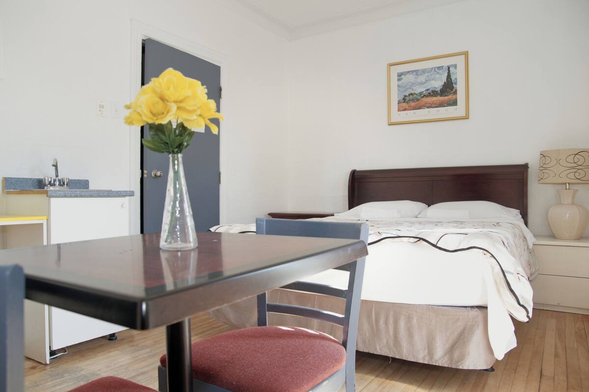 Une chambre à coucher avec un lit, une table de chevet, une chaise et un vase de fleurs.