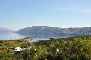 A coastal landscape with a clear view of a lake, hills in the background, and a building with a white roof in the foreground.