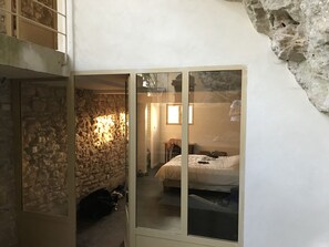 Un dormitorio con pared de piedra, cama, armario y ventana pequeña.