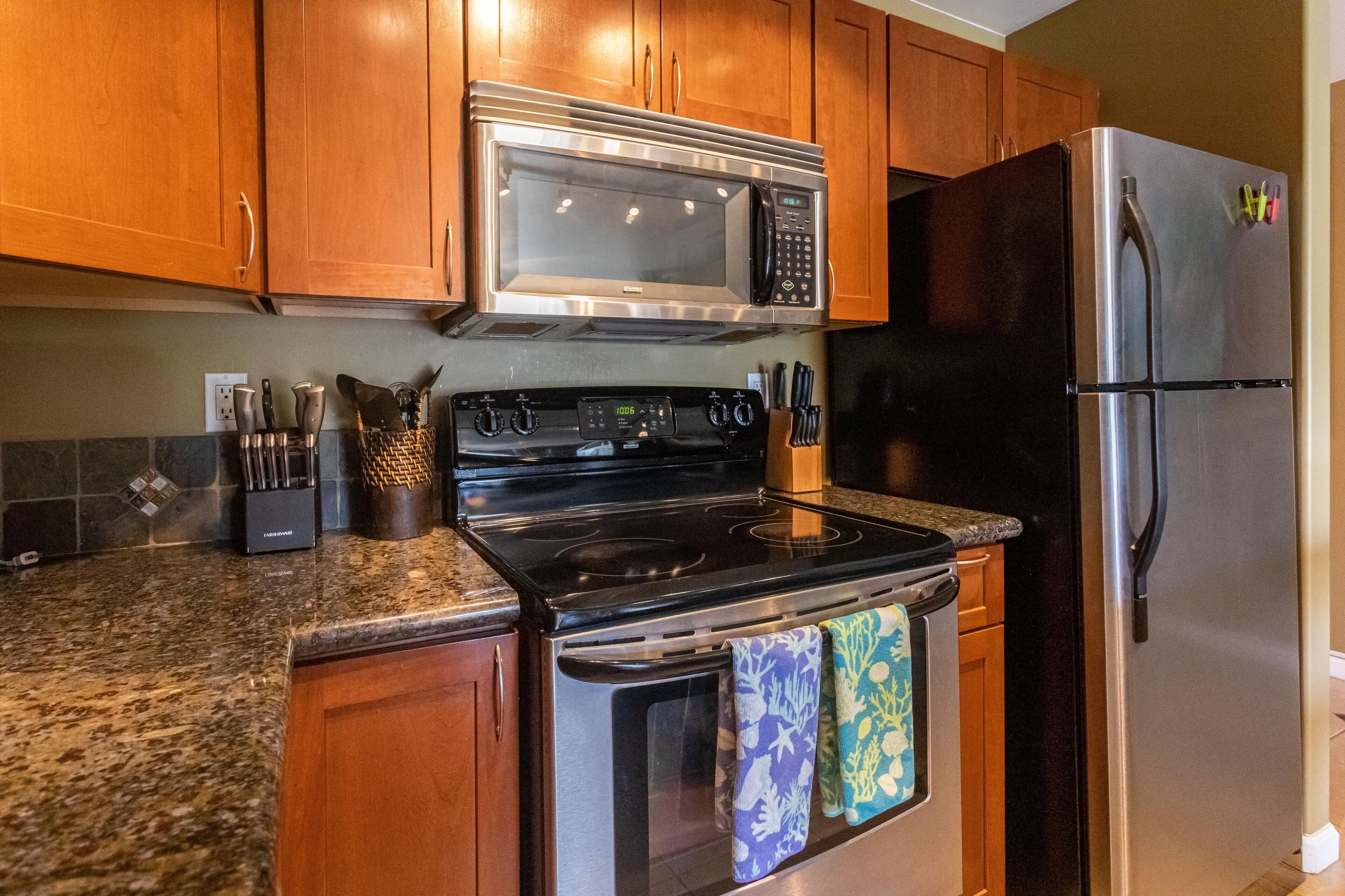 A kitchen with wooden cabinets, a stainless steel microwave, a black stove, and a stainless steel refrigerator.