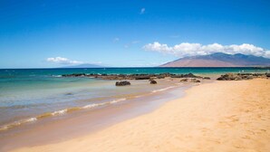 A beach with clear blue water, sandy shore, and rocky outcrops. - Hale Kamaole 127 Ground floor condo, easy access to best beach on Maui! (Kihei)