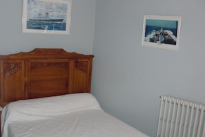 A bedroom with a wooden headboard, a white bedspread, a white radiator, and two framed pictures on the wall.