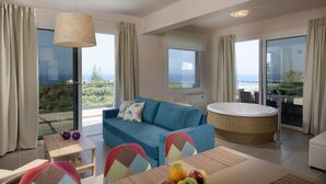 A modern hotel room with a blue sofa, a round bathtub, and a dining area with a fruit bowl.