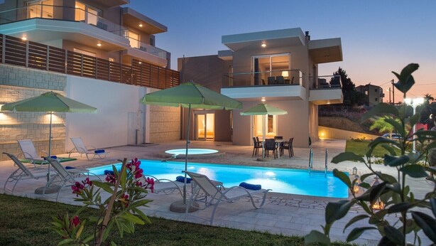 A modern two-story house with a swimming pool, outdoor seating, and a well-lit patio area.