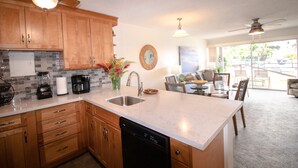 A modern kitchen with wooden cabinets, a dishwasher, and a coffee maker. There is a dining area with a table and chairs. - #128 Ground floor condo, easy access to best beach on Maui! (Kihei)