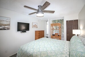 A bedroom with a bed, a ceiling fan, a TV, a wooden wardrobe, and a window with blinds. - #128 Ground floor condo, easy access to best beach on Maui! (Kihei)