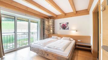 Une chambre dotée d’un grand lit, de poutres en bois, d’un mur en pierre et d’un balcon offrant une vue sur la verdure.