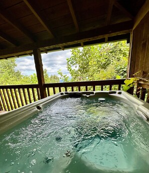 A hot tub under a wooden deck with a view of lush greenery and trees.