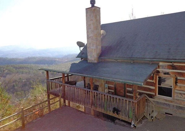 A wooden cabin with a stone chimney, a covered deck, and a scenic view of the mountains.