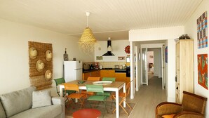 A modern living room with a sofa, dining table, and chairs. A kitchen is visible in the background with a hanging light fixture. - Flat for 6 on the main beach, St Gilles (Saint-Gilles-Croix-de-Vie)