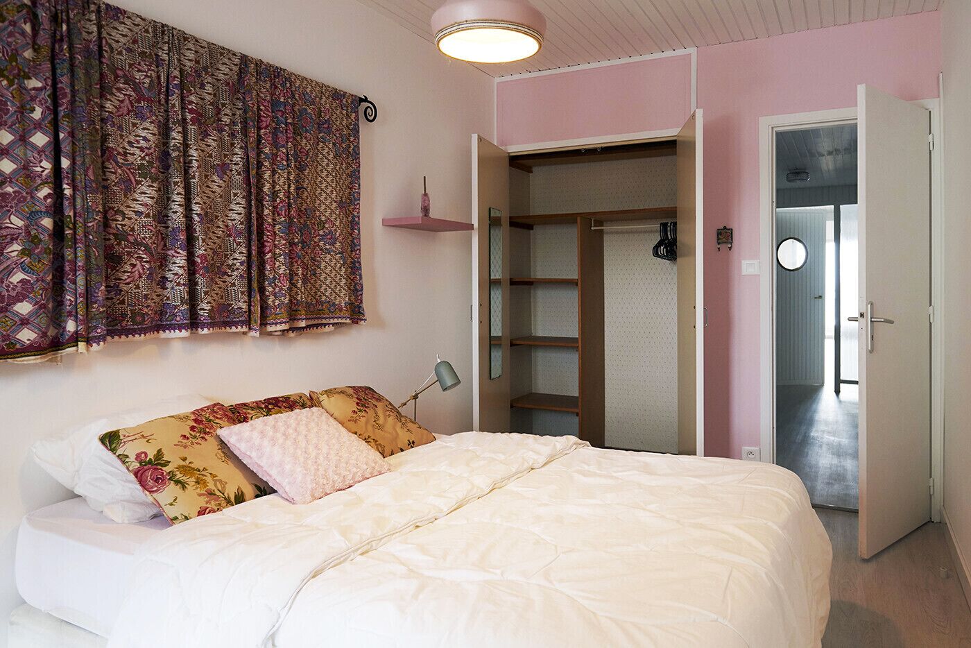 Un dormitorio con cama, armario, espejo y puerta que da a otra habitación.