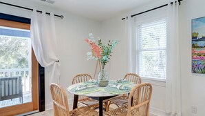 Un comedor con una mesa redonda, cuatro sillas de mimbre, un florero con flores y un cuadro en la pared.