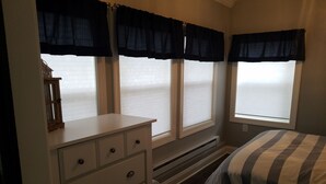 A bedroom with a bed, a dresser, and three windows with dark curtains. - Paradise in Port Bay (Wolcott)
