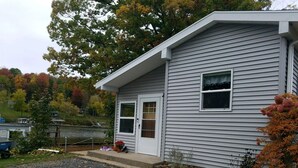 A two-story house with a front porch, a garage, and a small garden area with autumn foliage. - Paradise in Port Bay (Wolcott)