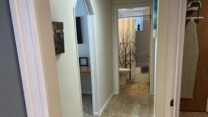 Een hal met houten vloer, witte wanden en een deur naar een badkamer met toilet en douche.