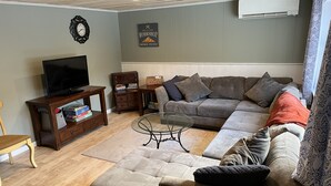 Een woonkamer met een hoekbank, een televisie, een salontafel en een wandklok.