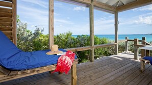 Eine Holzterrasse mit einer blauen gepolsterten Bank, einem Strohhut und einem roten Stoff.