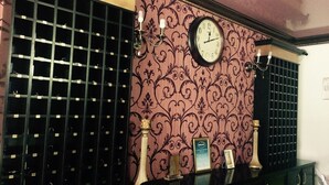 Ein Zimmer mit einer Wanduhr, einem gemusterten Wandteppich und einem schwarzen Schrank mit Schubladen.