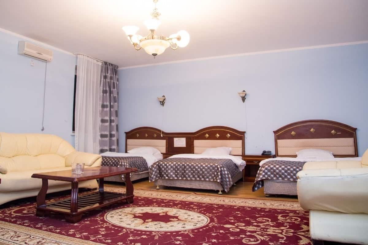 A hotel room with two beds, a sofa, a wooden coffee table, and a chandelier.