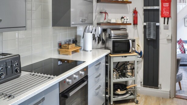 Uma cozinha moderna com fogão embutido, forno, micro-ondas e torradeira. Há uma tábua de corte de madeira e um suporte para facas na bancada.