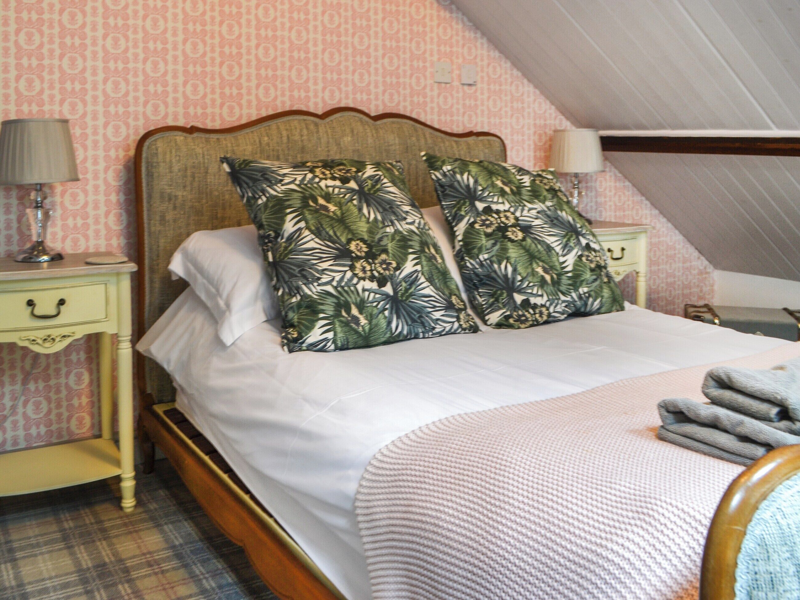 Une chambre à coucher avec un lit, deux tables de chevet, une lampe, une valise et un tapis à motifs écossais.